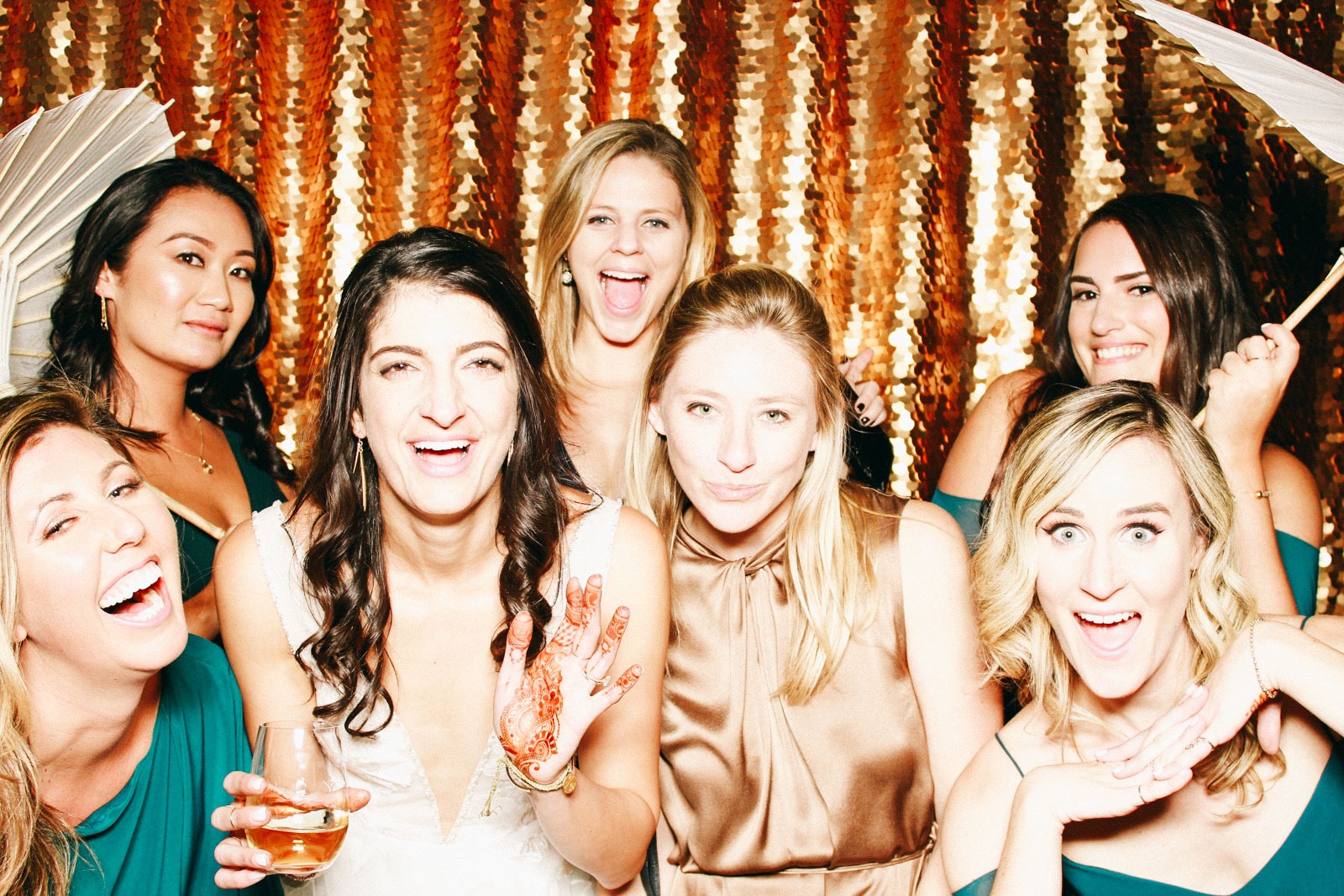 A group photo of a bride and her bridesmaids against a gold sequin backdrop from Hive Photo Booth rentals.